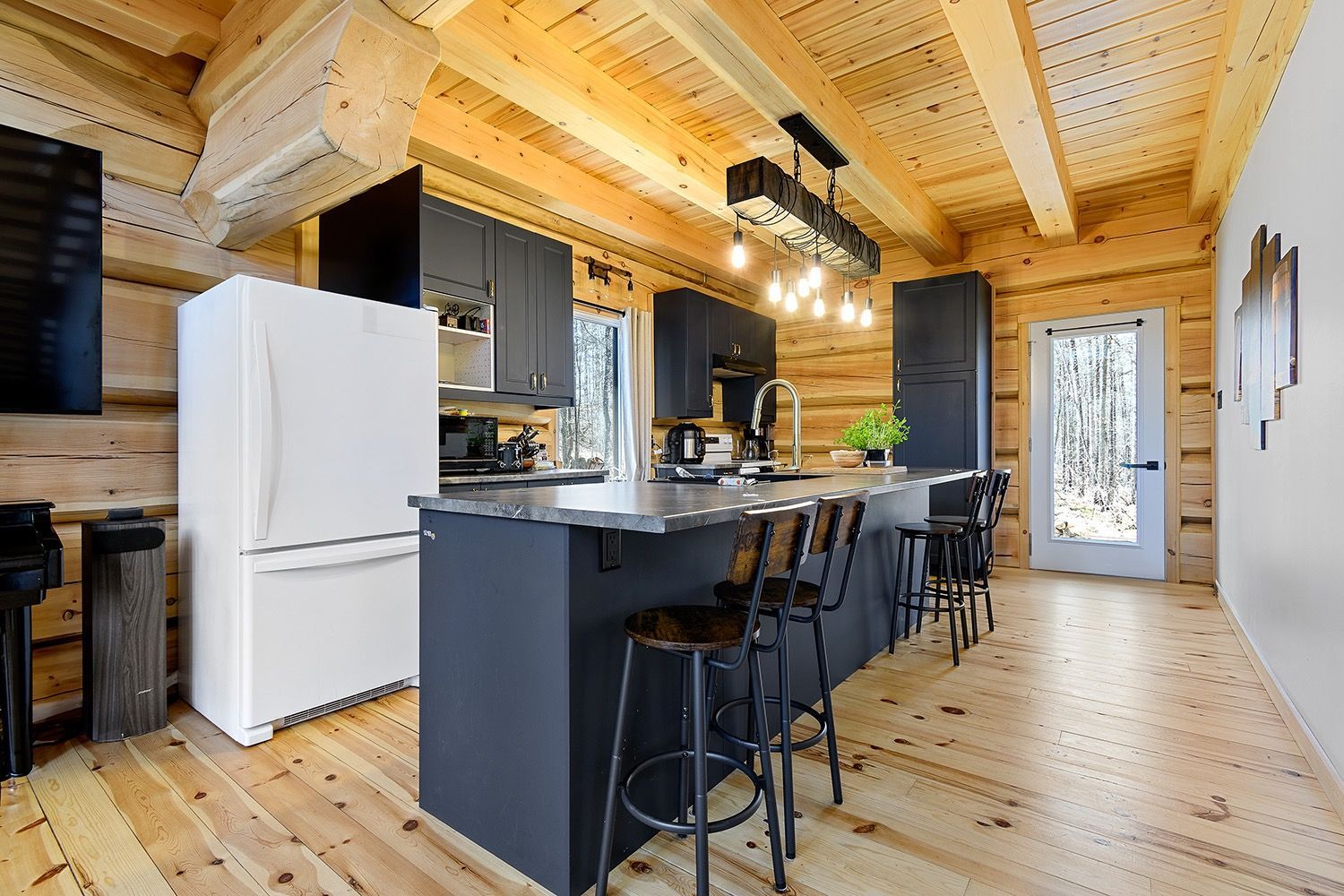 Modern kitchen with wood ceiling, black island, white fridge, and bar stools