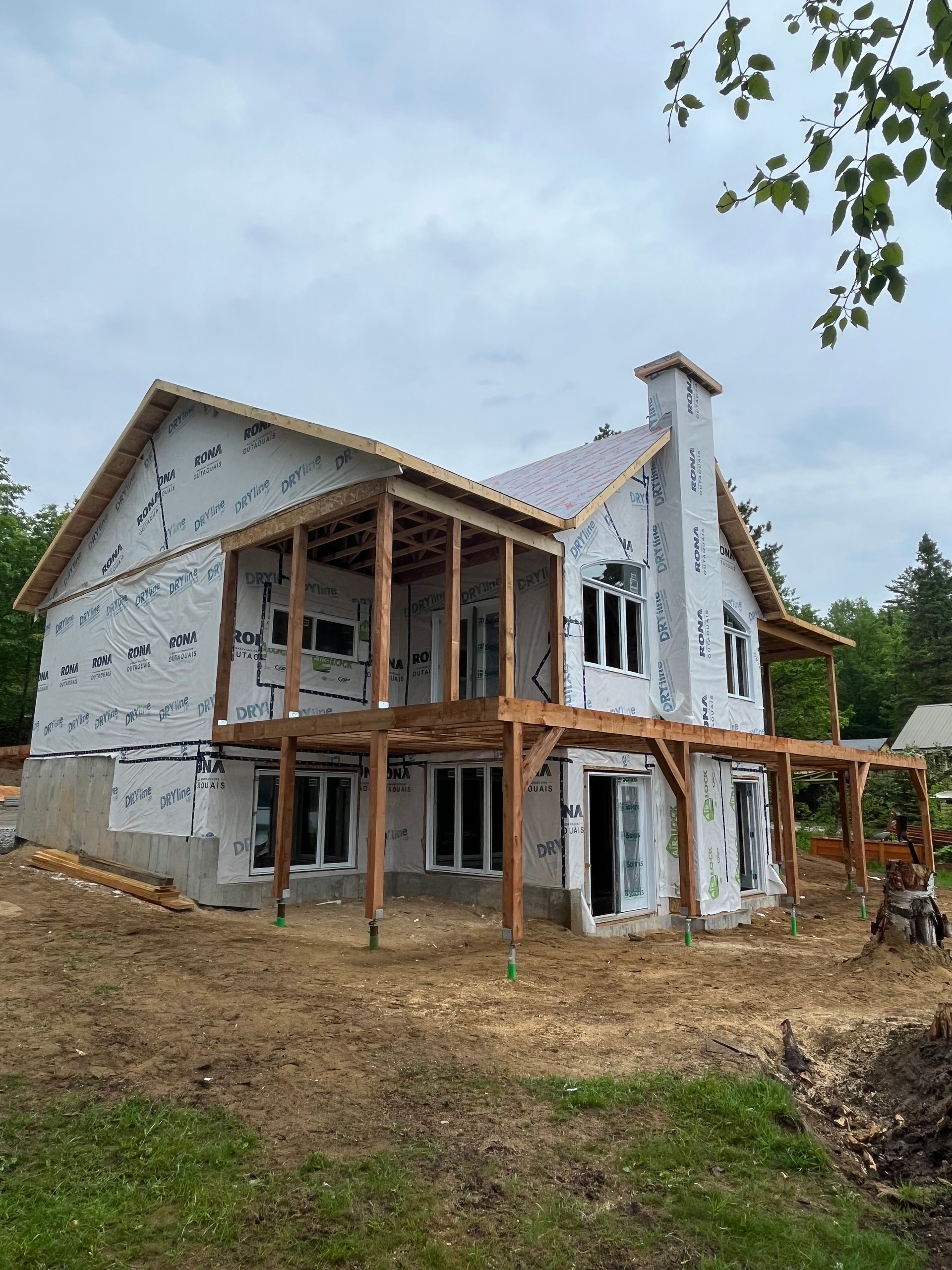 Partially built two-story house under construction with exposed wood framing and gray exterior wrap