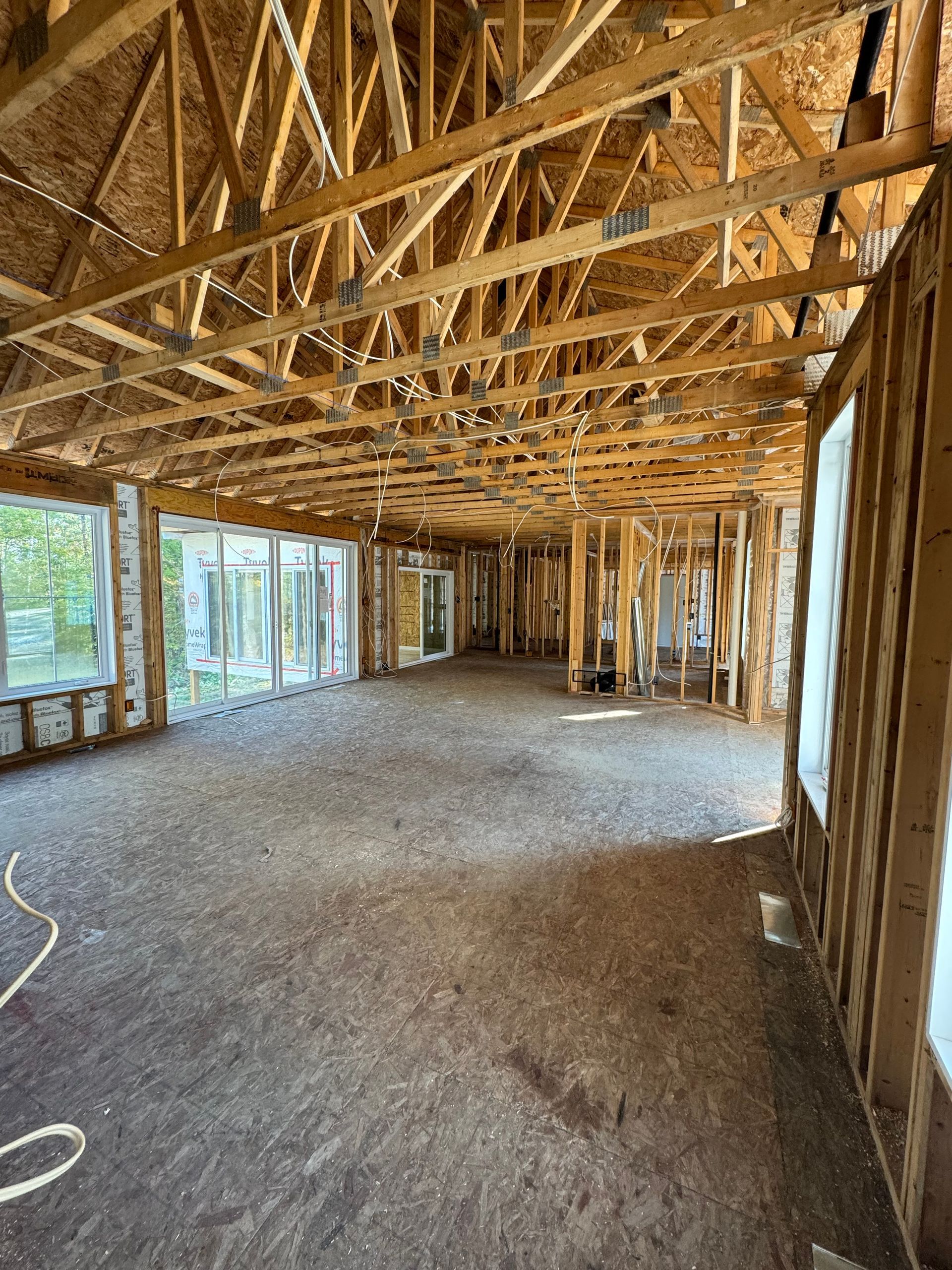 Unfinished interior of a house with exposed wood framing, trusses, and large windows.