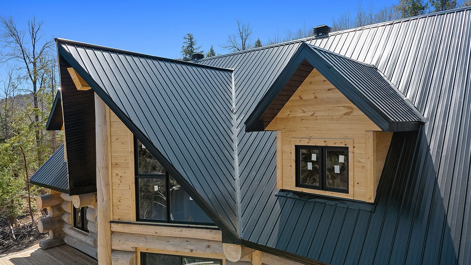 Modern house roof with dark metal panels and two dormer windows under a blue sky