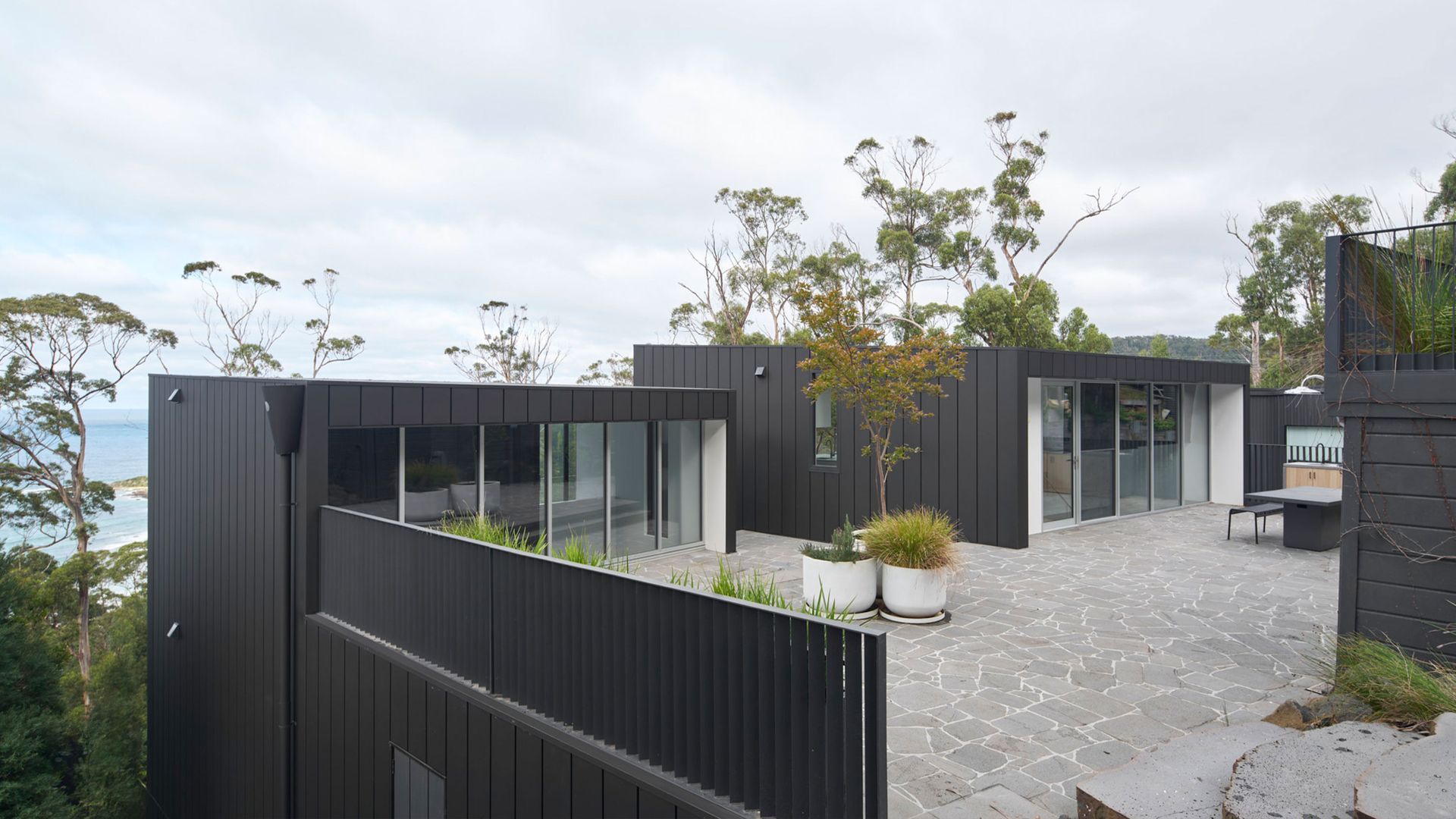 A large black house with a lot of windows is sitting on top of a hill.