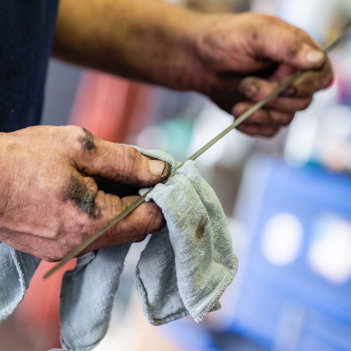 Mechanic wiping a dipstick with a dirty rag to check engine oil level.