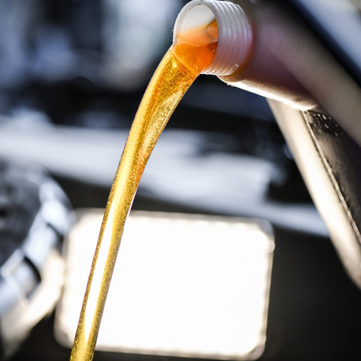 Motor oil pouring from a white bottle into a car engine.