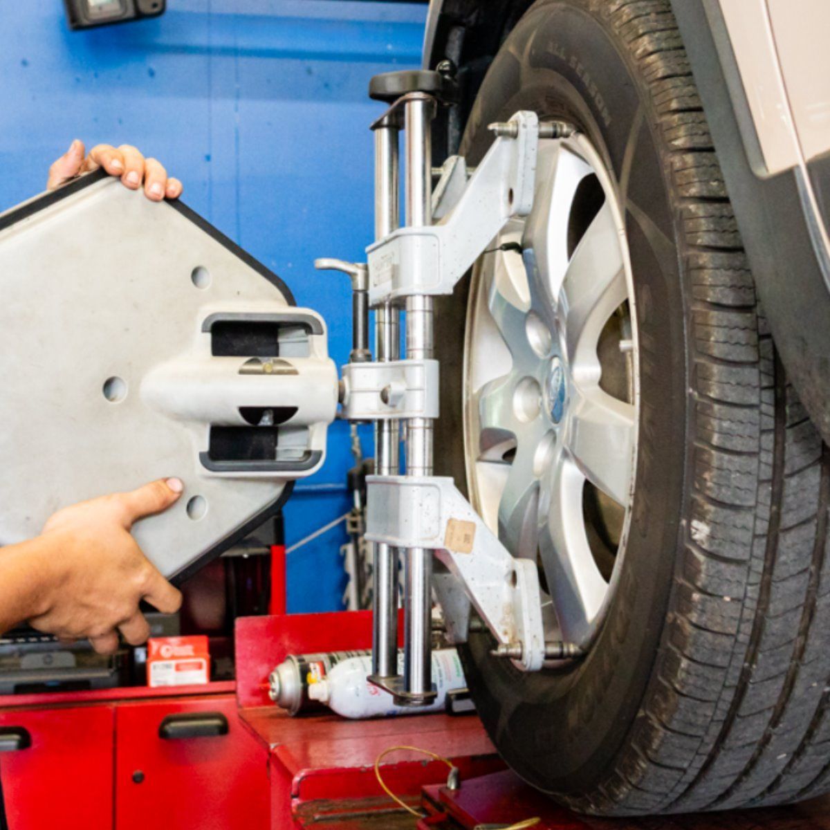A mechanic aligning a car wheel with alignment equipment in a shop.