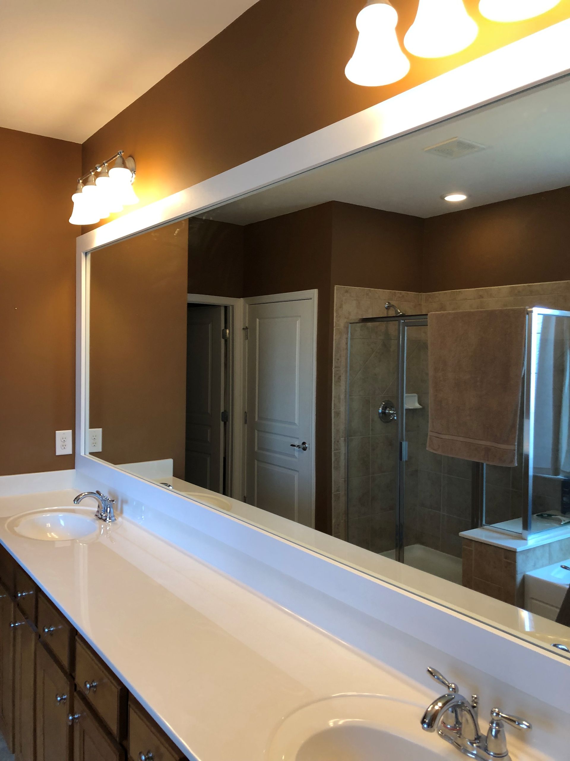 Bathroom vanity with large mirror, double sinks, and glass shower reflected in the mirror.