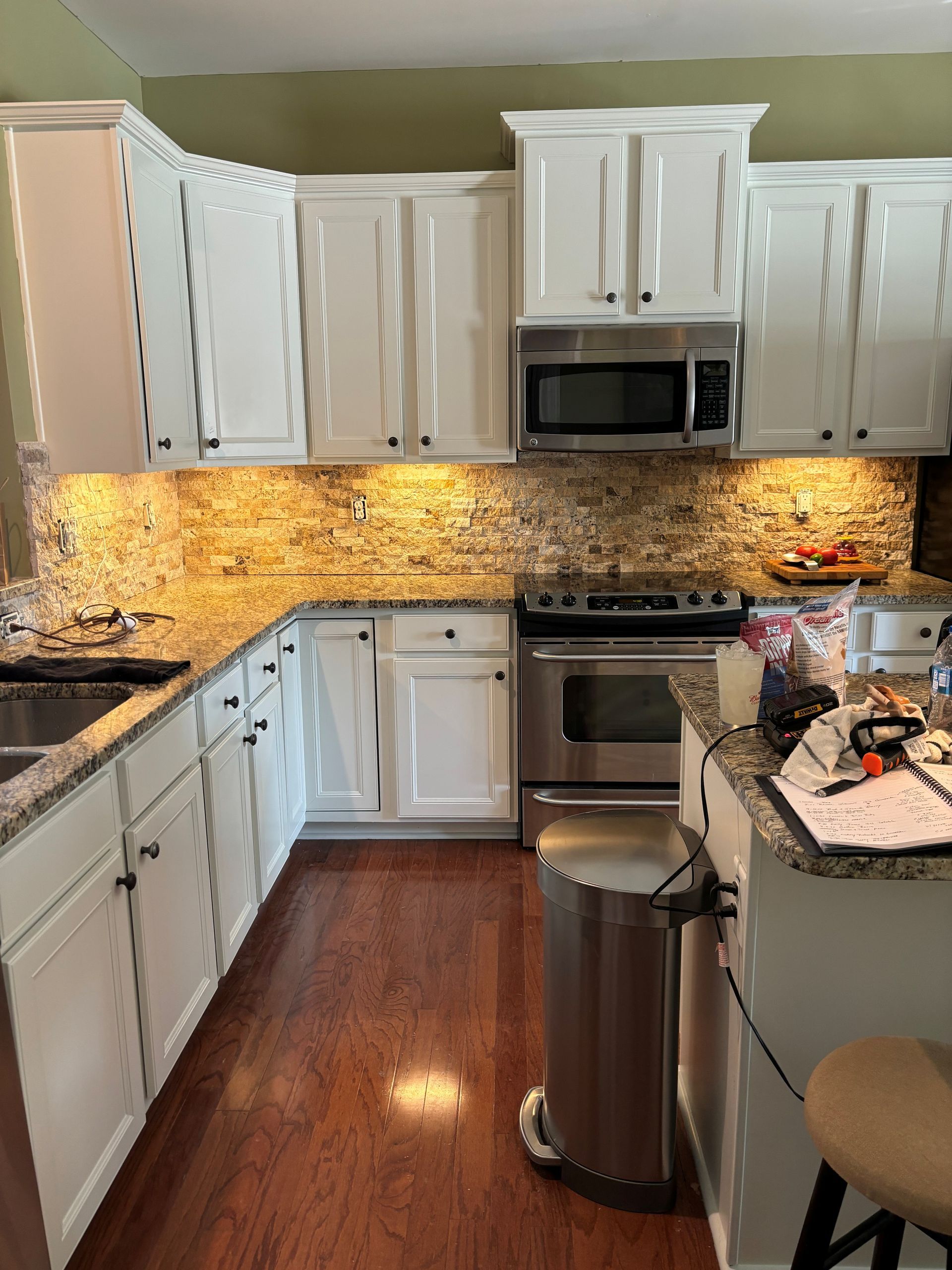 White kitchen with cabinets, stainless appliances, granite counters, and warm under-cabinet lighting.