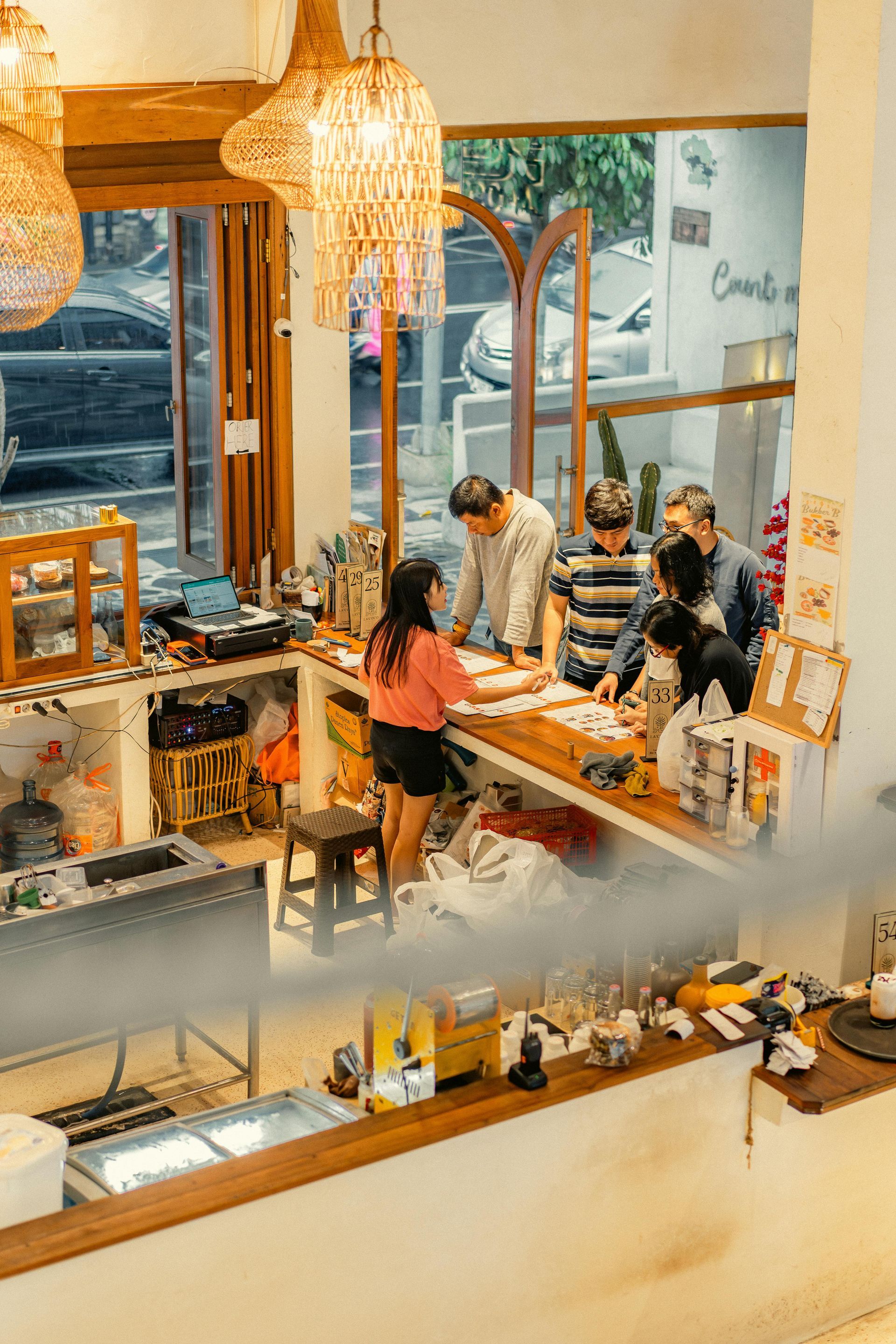 People gathered at a cozy café counter with warm lighting and hanging wicker lamps.