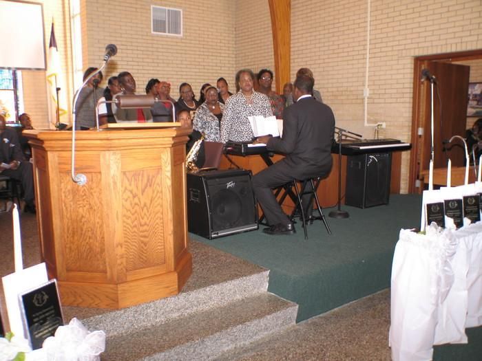 Choir singing in a church with a pianist at a keyboard beside a wooden pulpit