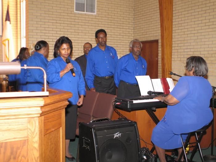 Four people in blue sing and play keyboard during a church service indoors
