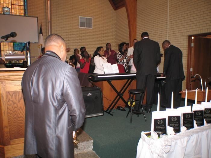 People gathered in a church hall for a ceremony, with a keyboard, speakers, and awards on a table.