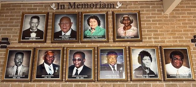 Memorial wall with framed portraits of 10 people on a brick background and “In Memoriam” above