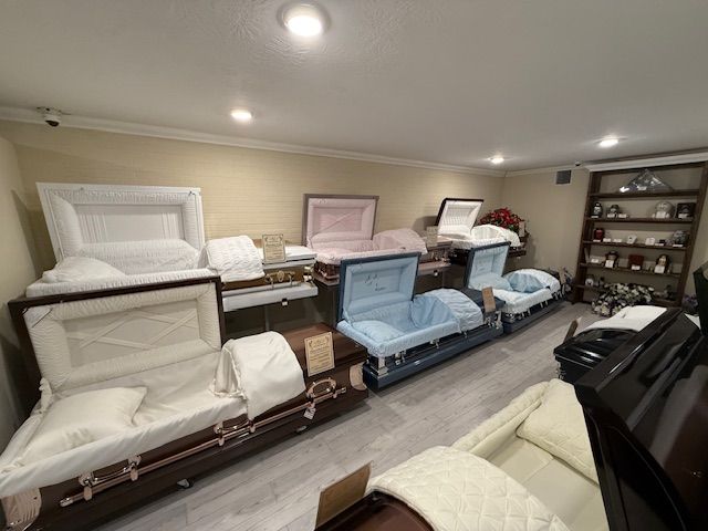 Funeral showroom with several open caskets in white, pink, blue, and brown under ceiling lights