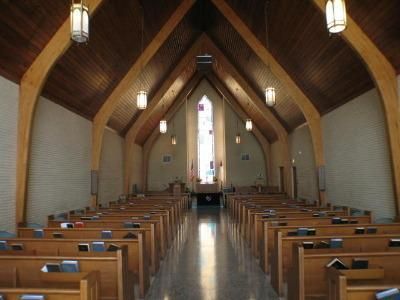 Empty church interior with wooden pews, high arched ceiling, and central stained-glass window