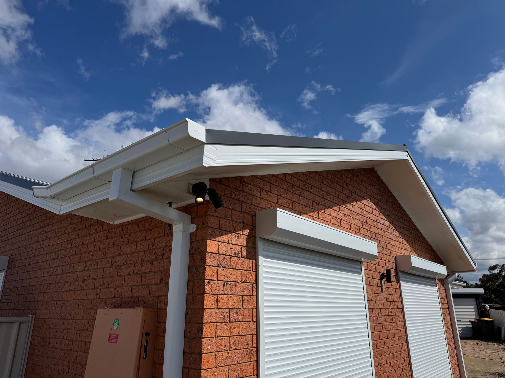 Red brick house with white trim, gutters, and security lights; blue sky with clouds — All Top Roofing In Woden, ACT