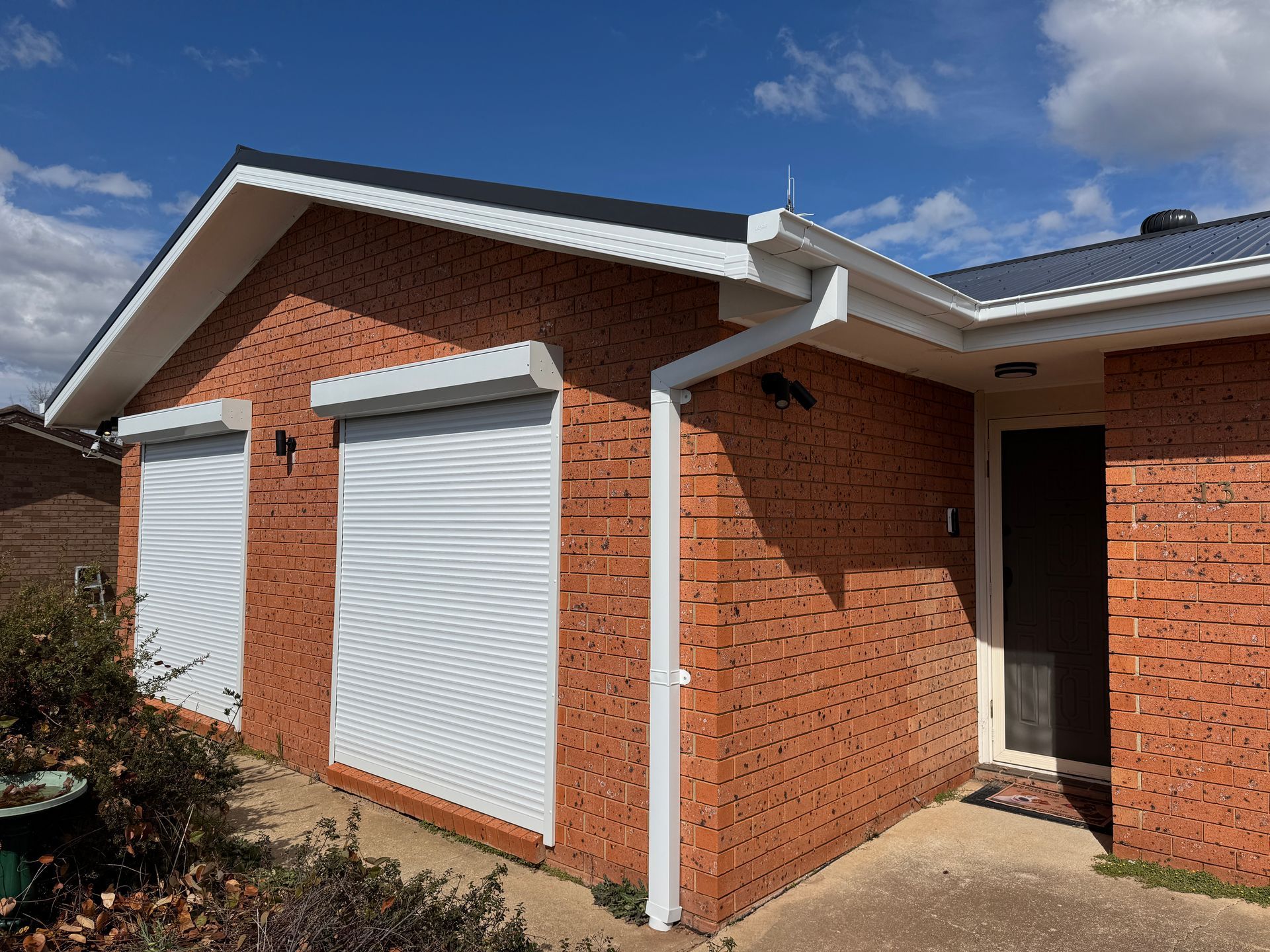 Brick house with white window shutters closed and a dark roof under a blue sky — All Top Roofing In Royalla, NSW