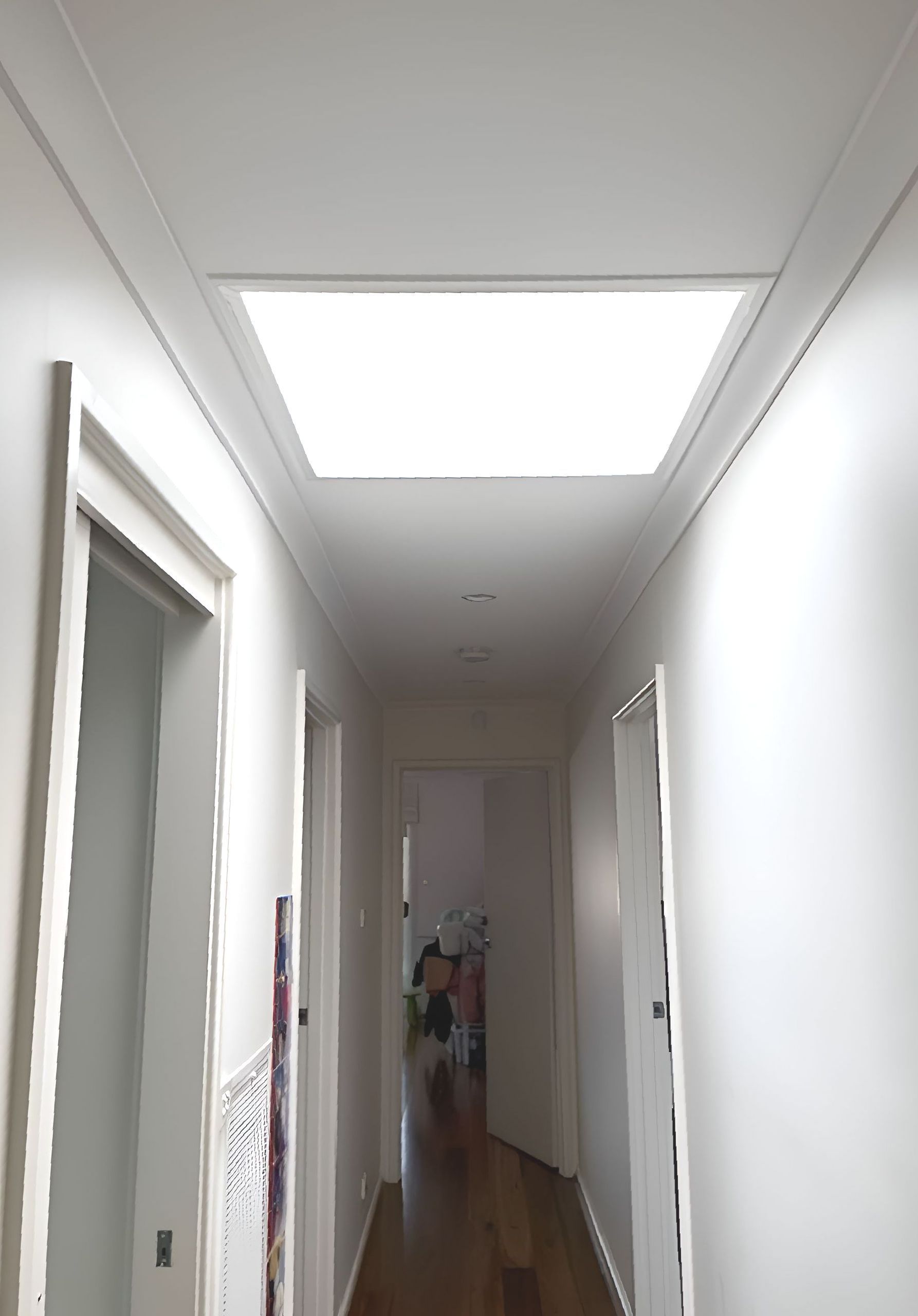 Long hallway with white walls, doors, and ceiling light. A bright light source in the ceiling illuminates the space — All Top Roofing In Tuggeranong, ACT