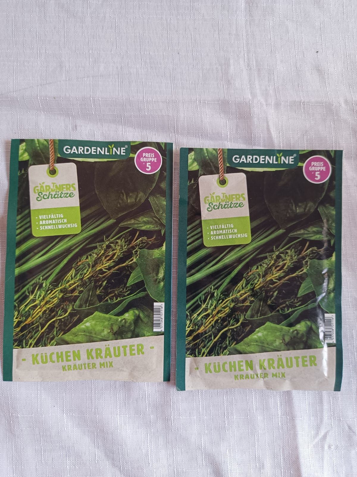 Two Gardenline kitchen herb seed packets on a light fabric background