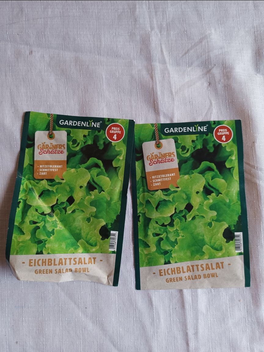 Two green lettuce seed packets on a light fabric surface