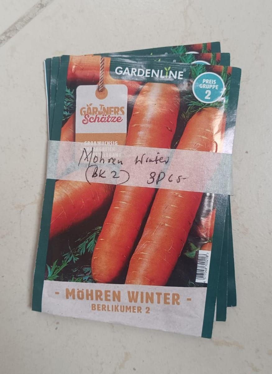 Stacked garden seed packets featuring carrots, with red, orange, and green packaging.