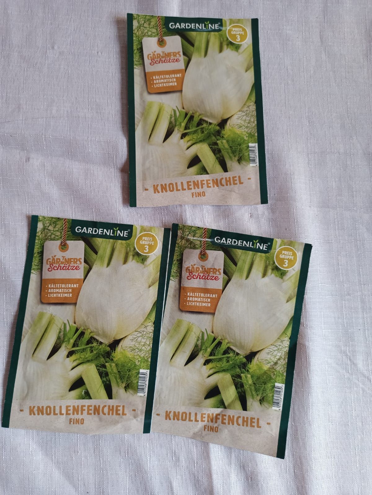 Three vegetable seed packets on a light cloth background, showing fennel bulbs.