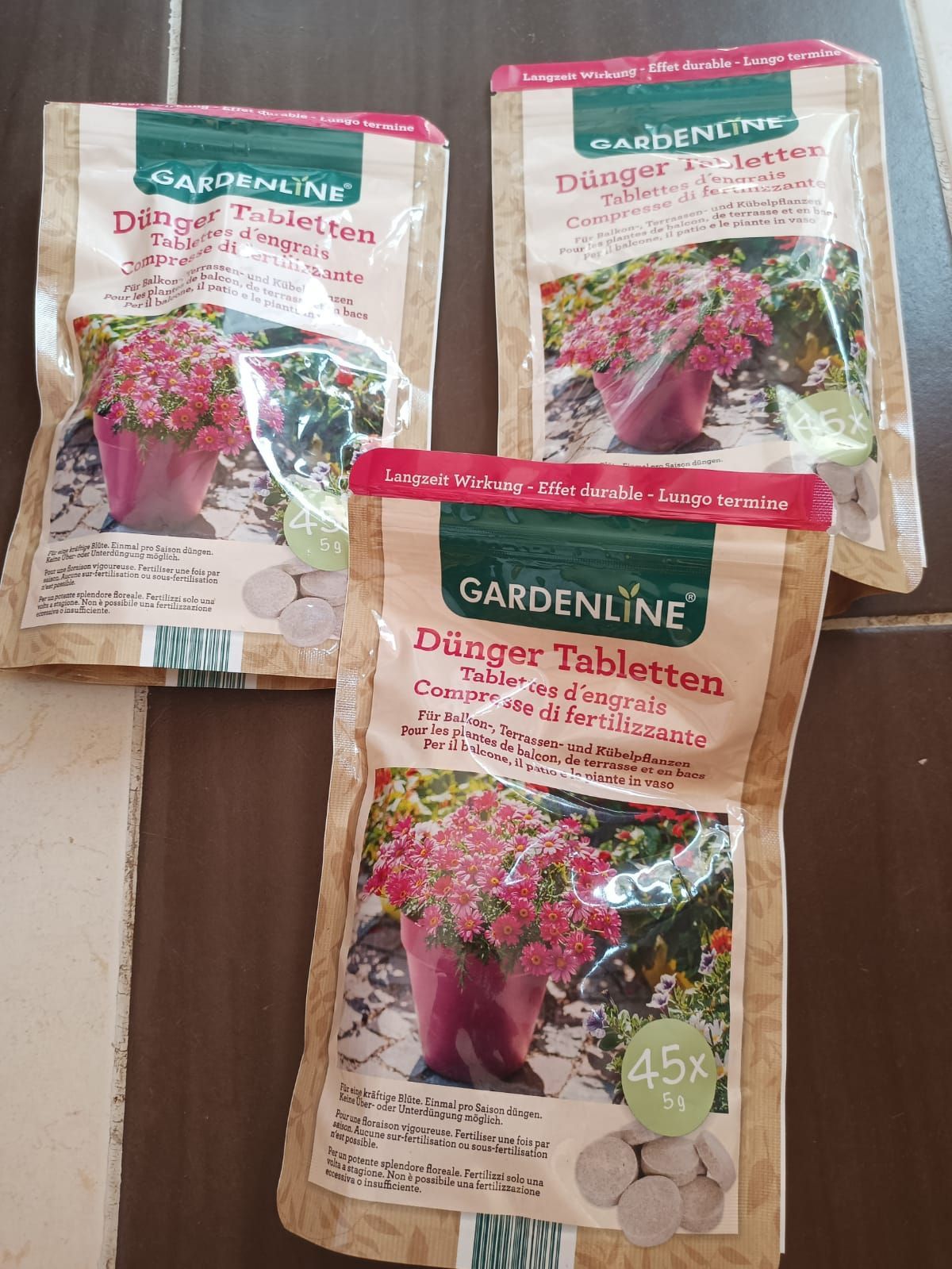 Three packets of Gardenline daisy flower seeds on a wooden surface