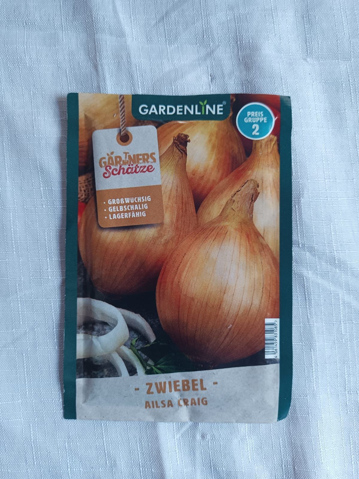 Gardenline onion seed packet with German text, showing yellow onions on a dark background