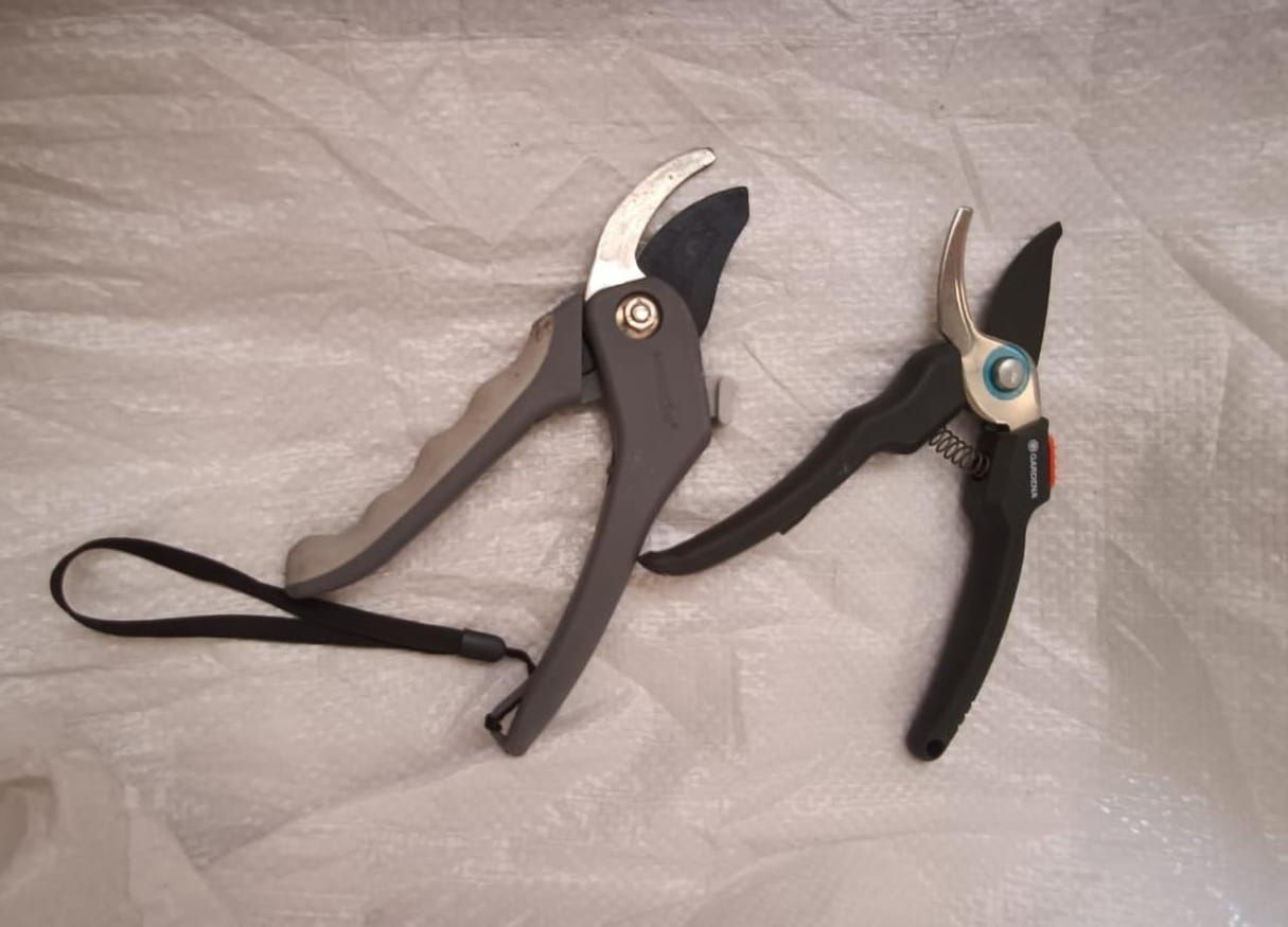 Two garden pruners on a light fabric surface, one gray and one black with teal accents.