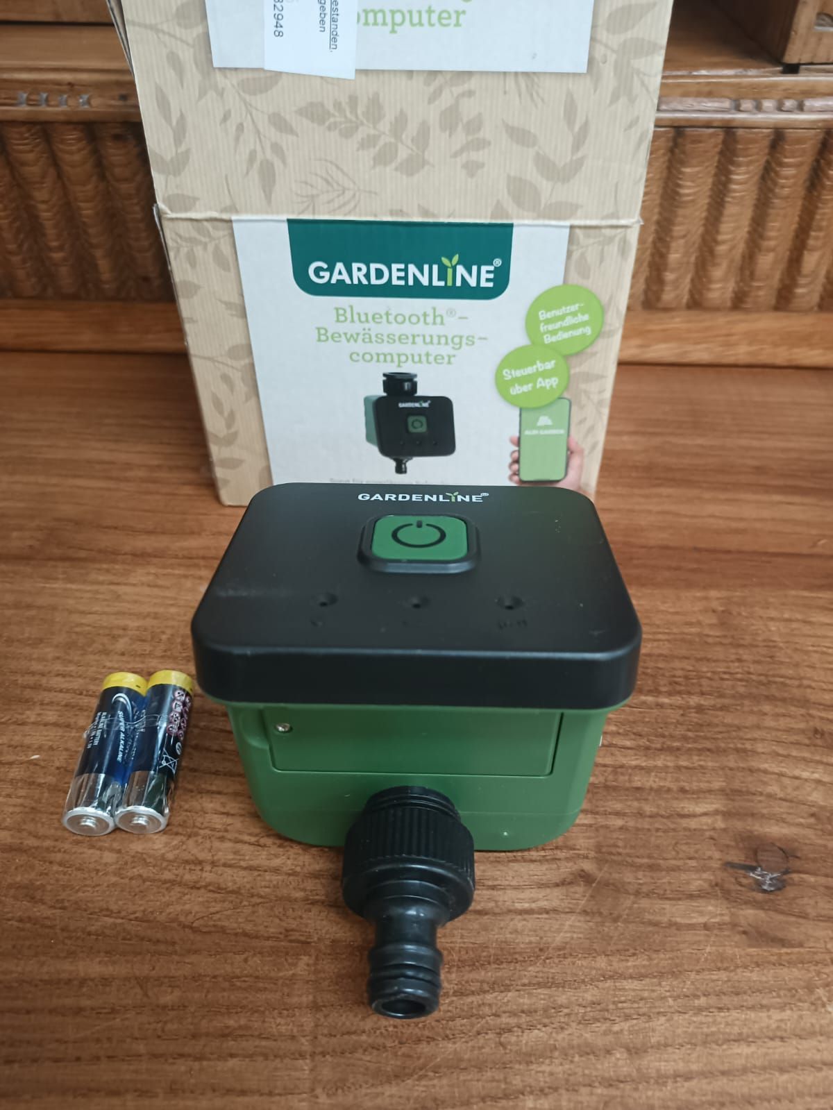 Green Gardenline irrigation timer with hose connector and batteries beside its box on a wooden table