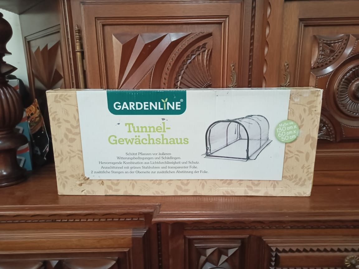 Gardenline Tunnel Gewächshaus box on a wooden cabinet, showing a small greenhouse illustration.