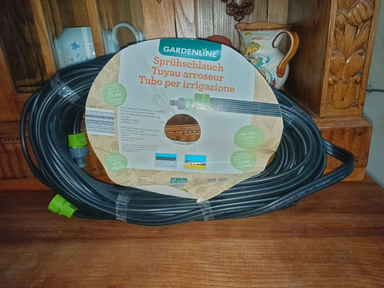 Coiled black garden hose with green connectors and label on a wooden shelf