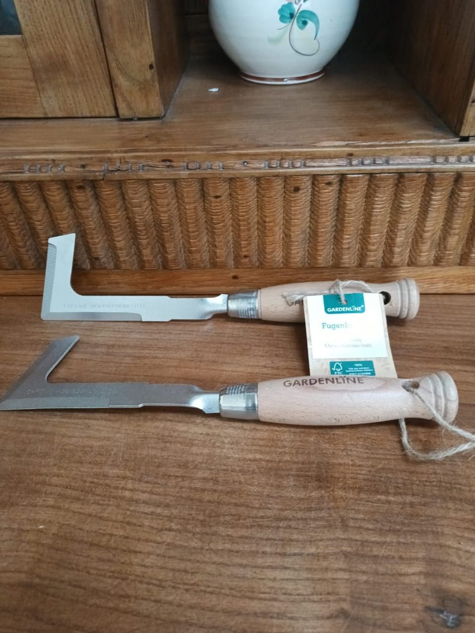 Two metal woodworking marking tools with white handles on a wooden shelf