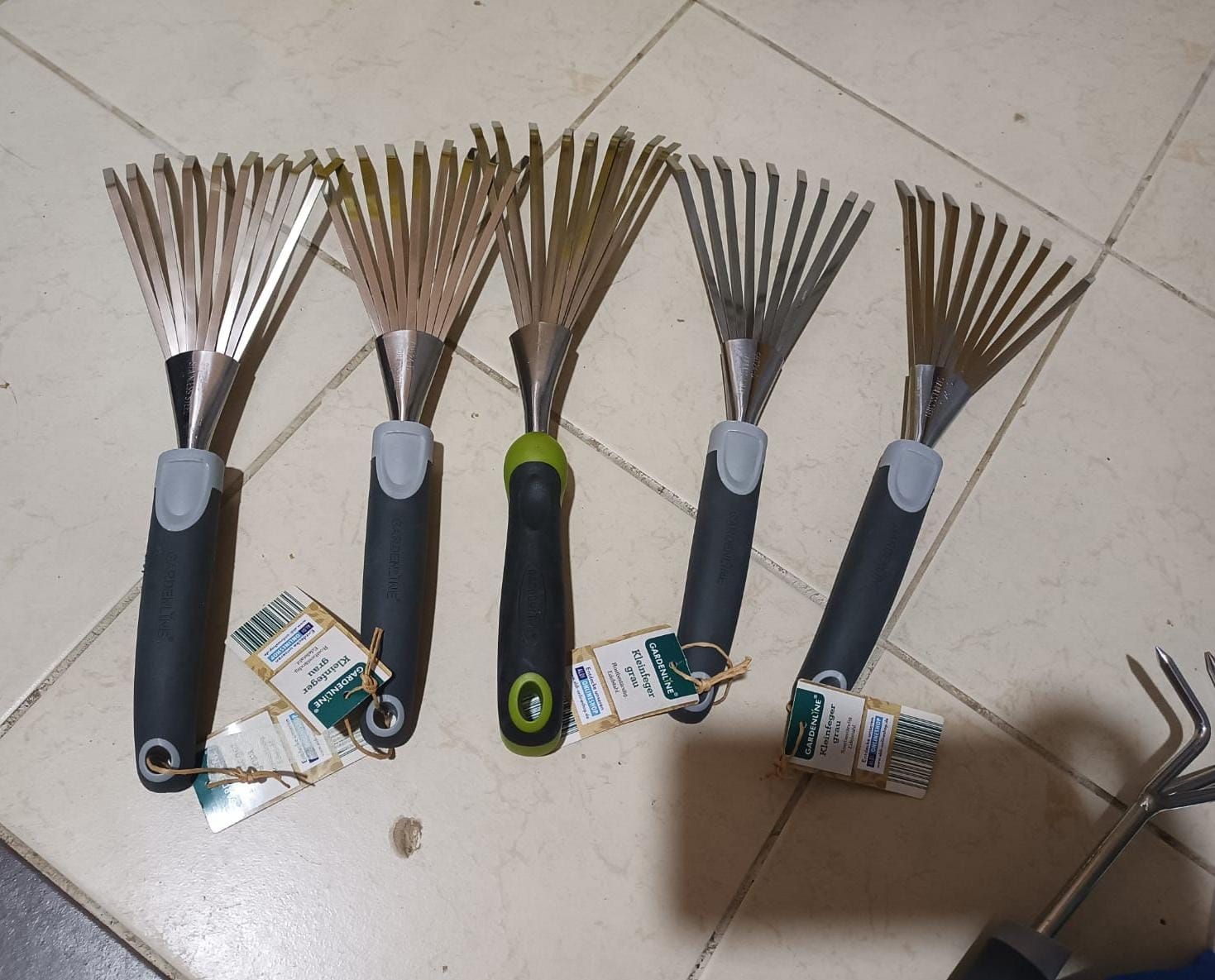 Five wire brushes with black handles on a tiled floor, plus loose brush heads and packaging.