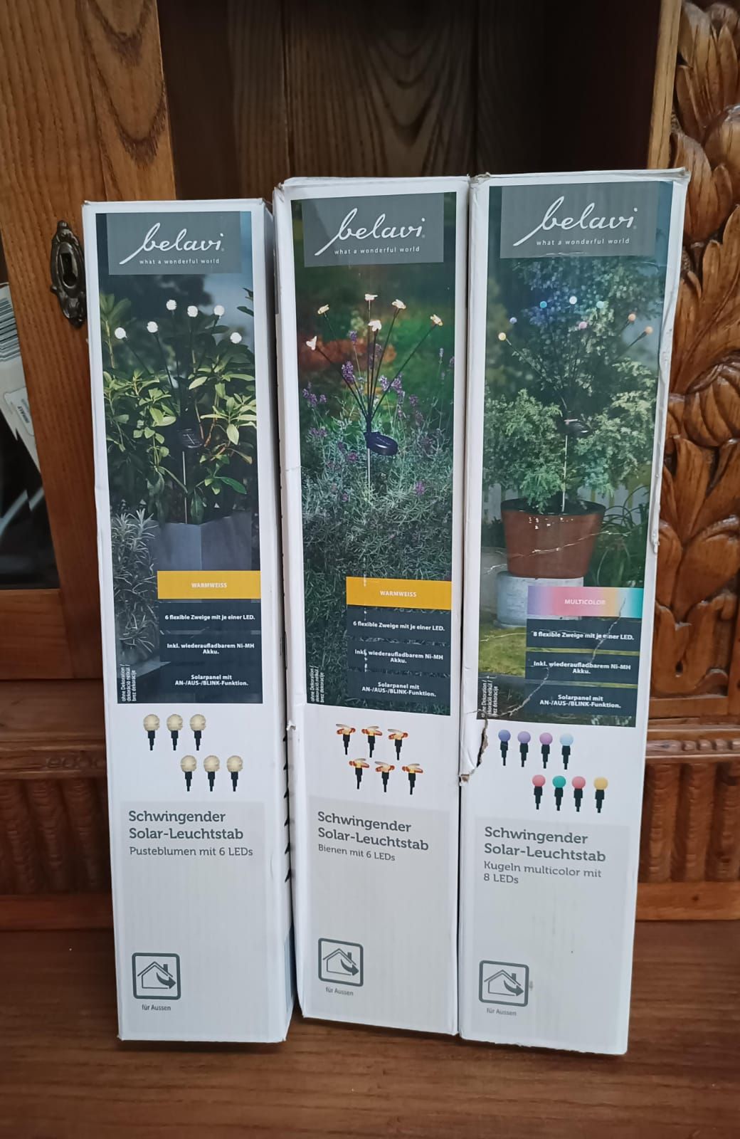 Three boxed solar garden lights with green foliage and flower images, standing on a wooden surface.