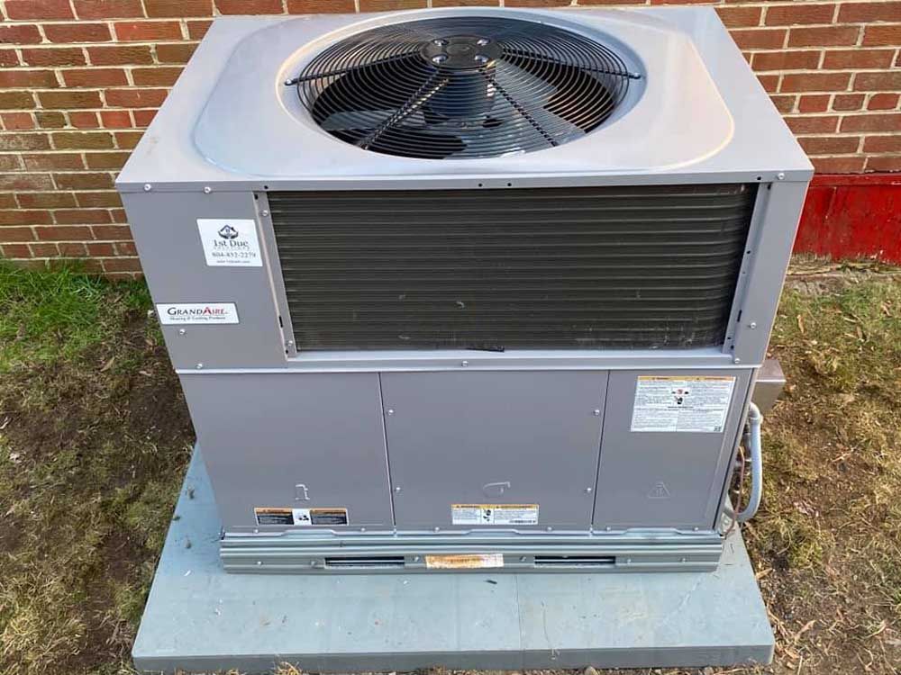 A large air conditioner is sitting on top of a concrete platform in front of a brick building.