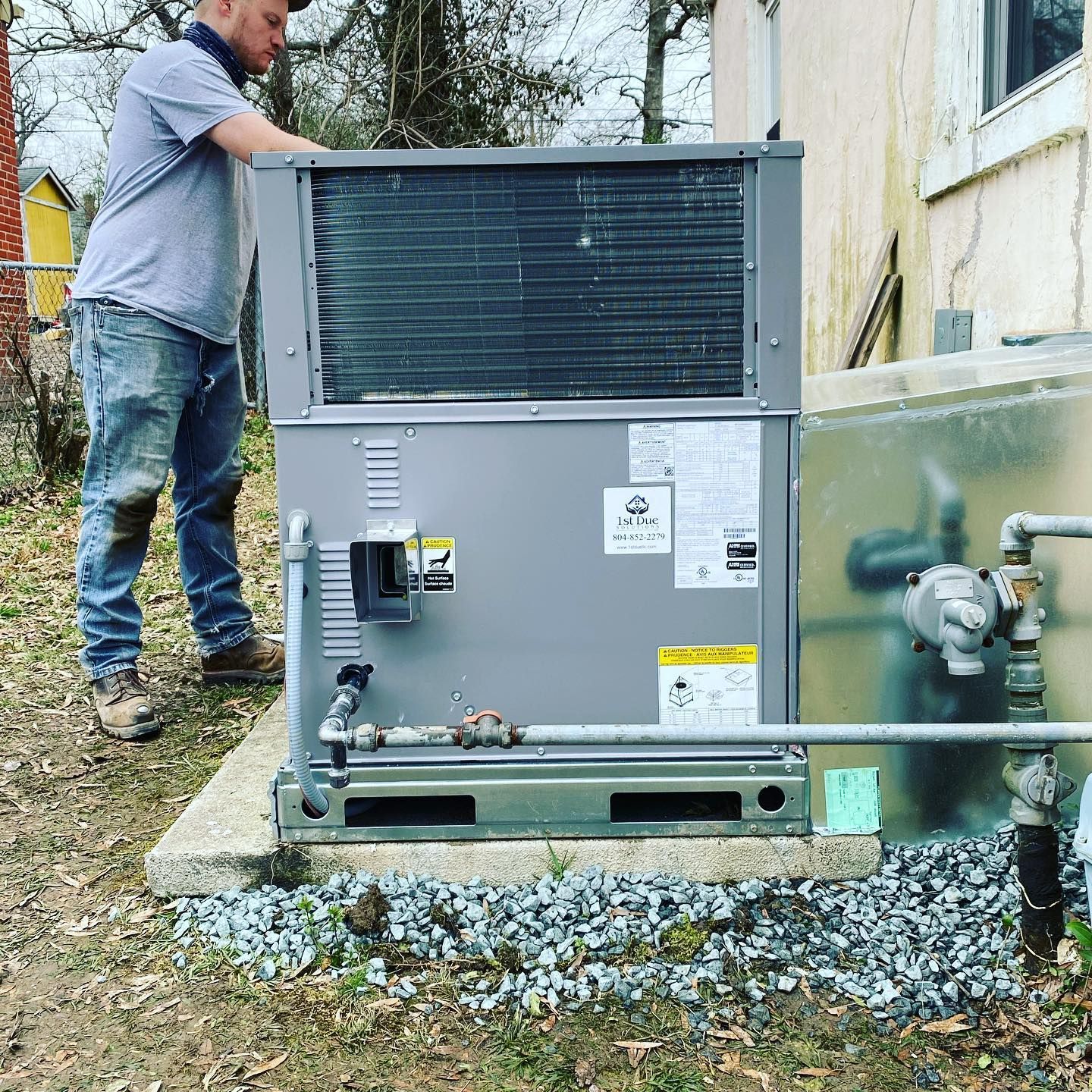 A man is working on an air conditioner outside of a house.