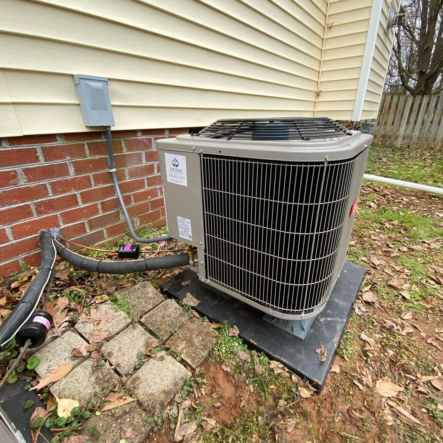 A large air conditioner is sitting on top of a gravel base in front of a brick wall.