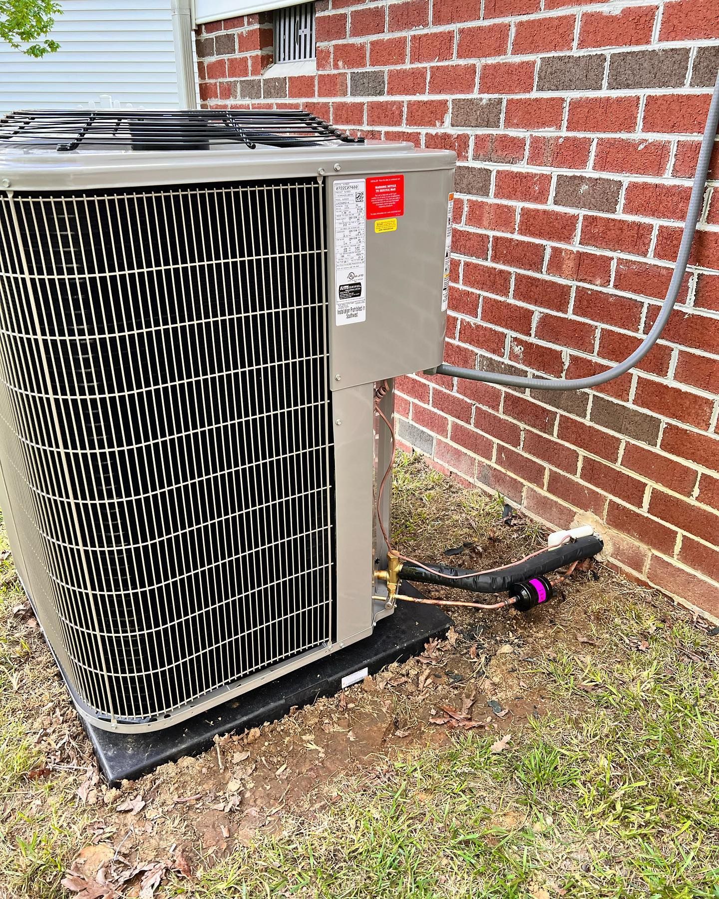 A large air conditioner is sitting outside of a brick building.