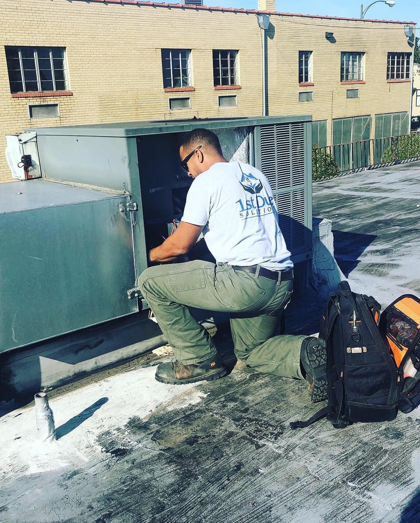 A man is working on an air conditioner on the roof of a building.