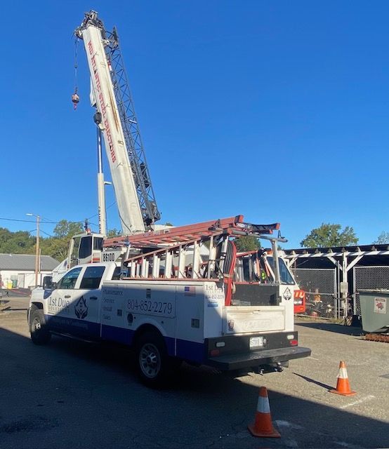 White crane truck with elevated boom, parked outside, against a blue sky. Orange safety cones visible.