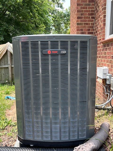 Gray Trane air conditioner unit next to a brick building.