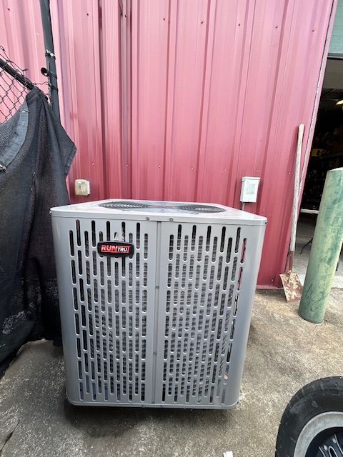 An air conditioning unit against a red wall with an electrical outlet, near a green pipe.