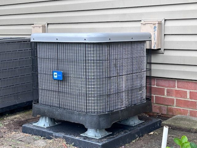 Outdoor HVAC unit with gray coils, a black base, and a blue control panel on a concrete pad.