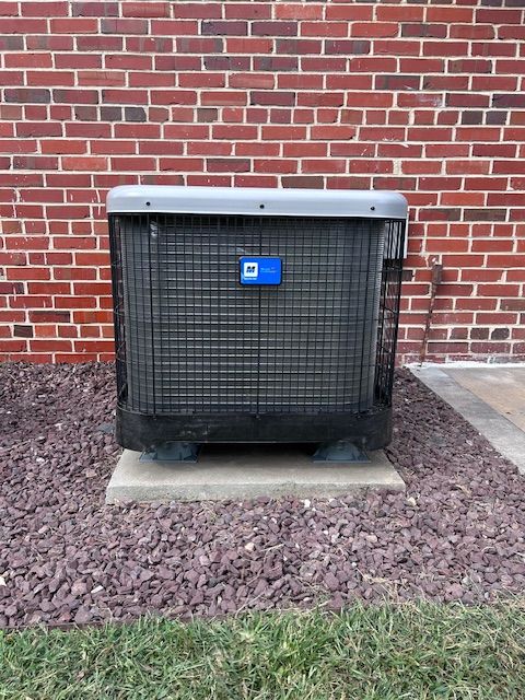 Air conditioning unit against a red brick wall. It is sitting on a concrete slab in a bed of rocks.