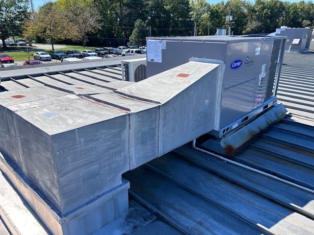 Carrier HVAC unit atop a commercial building roof. Silver metal ductwork and rooftop details. Sunny day.