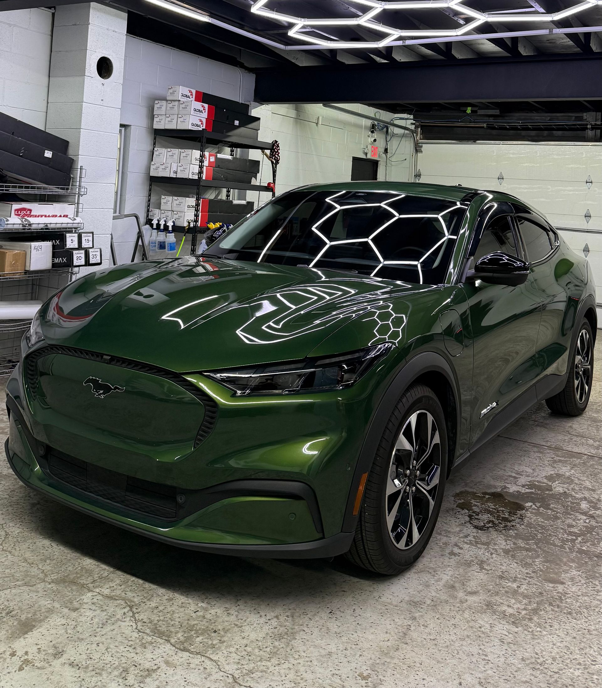 Green sports sedan in a garage, reflecting hexagonal ceiling lights on the hood and windshield.