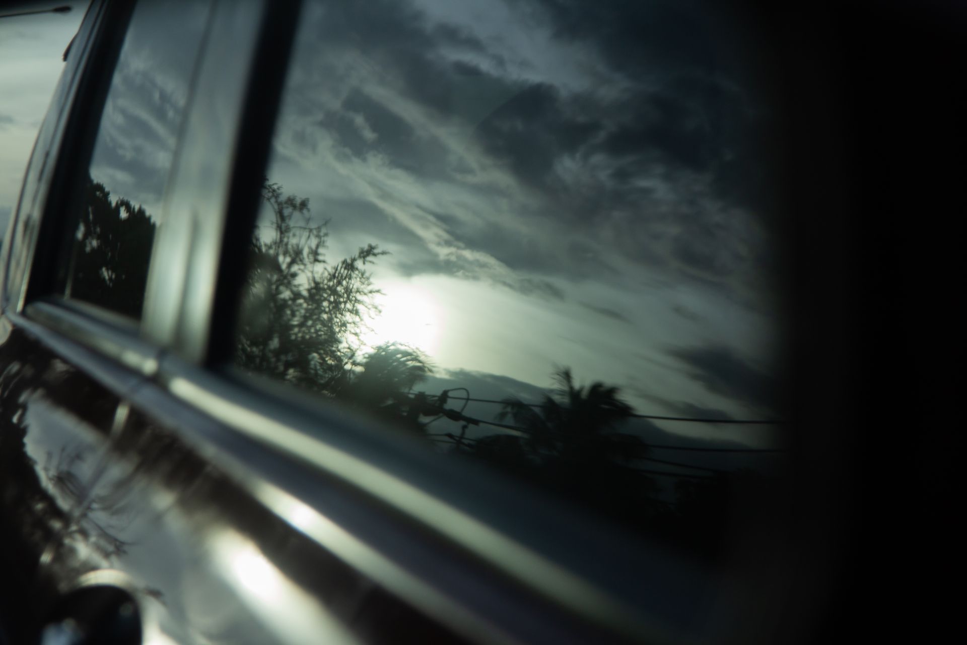 Sunset sky reflected in a car window, with dark clouds and silhouetted trees outside
