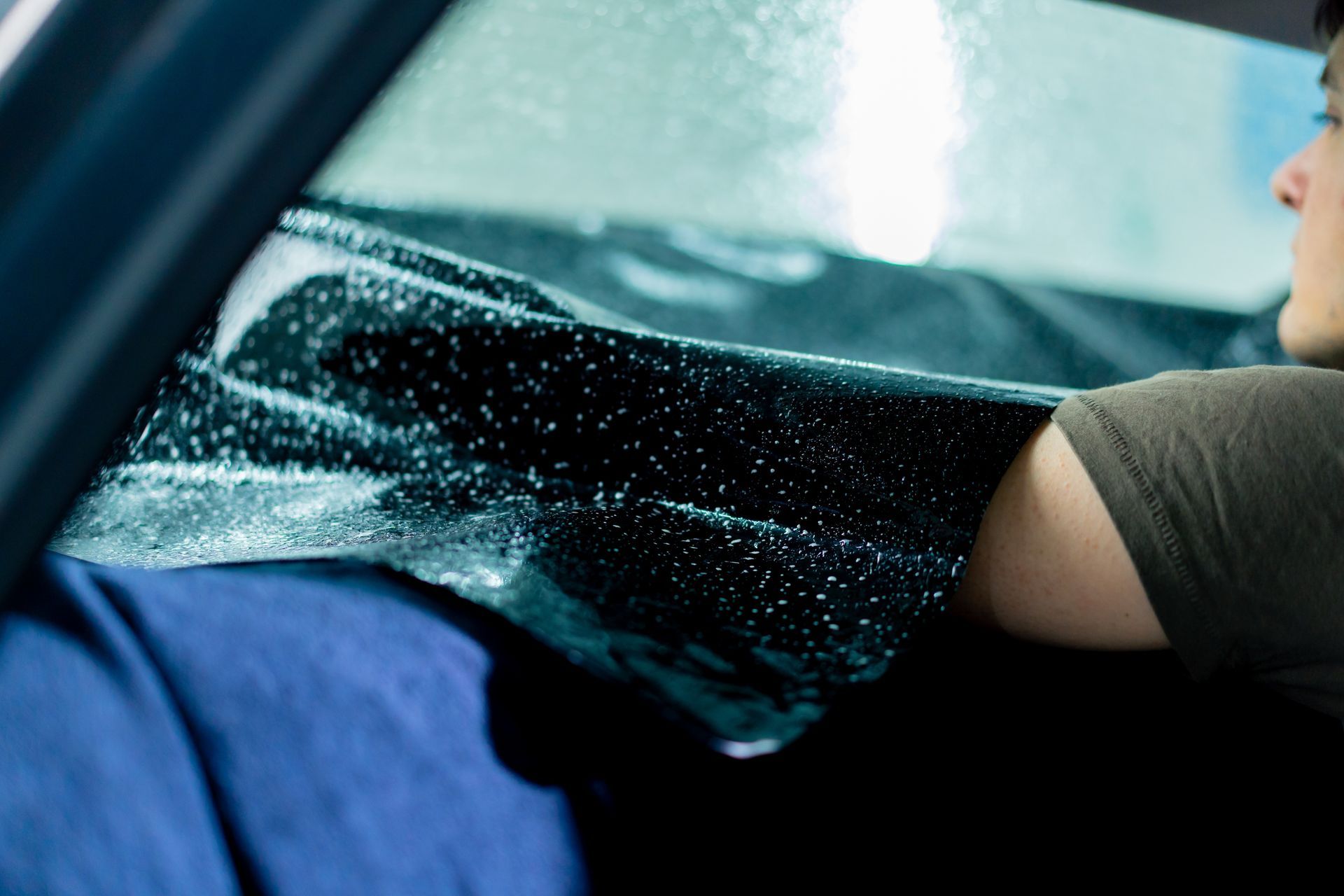 Person cleaning a car window with spray, blue seat visible inside the vehicle