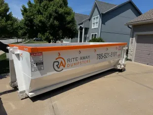 White and orange industrial dumpster on a rural property, likely for construction debris.