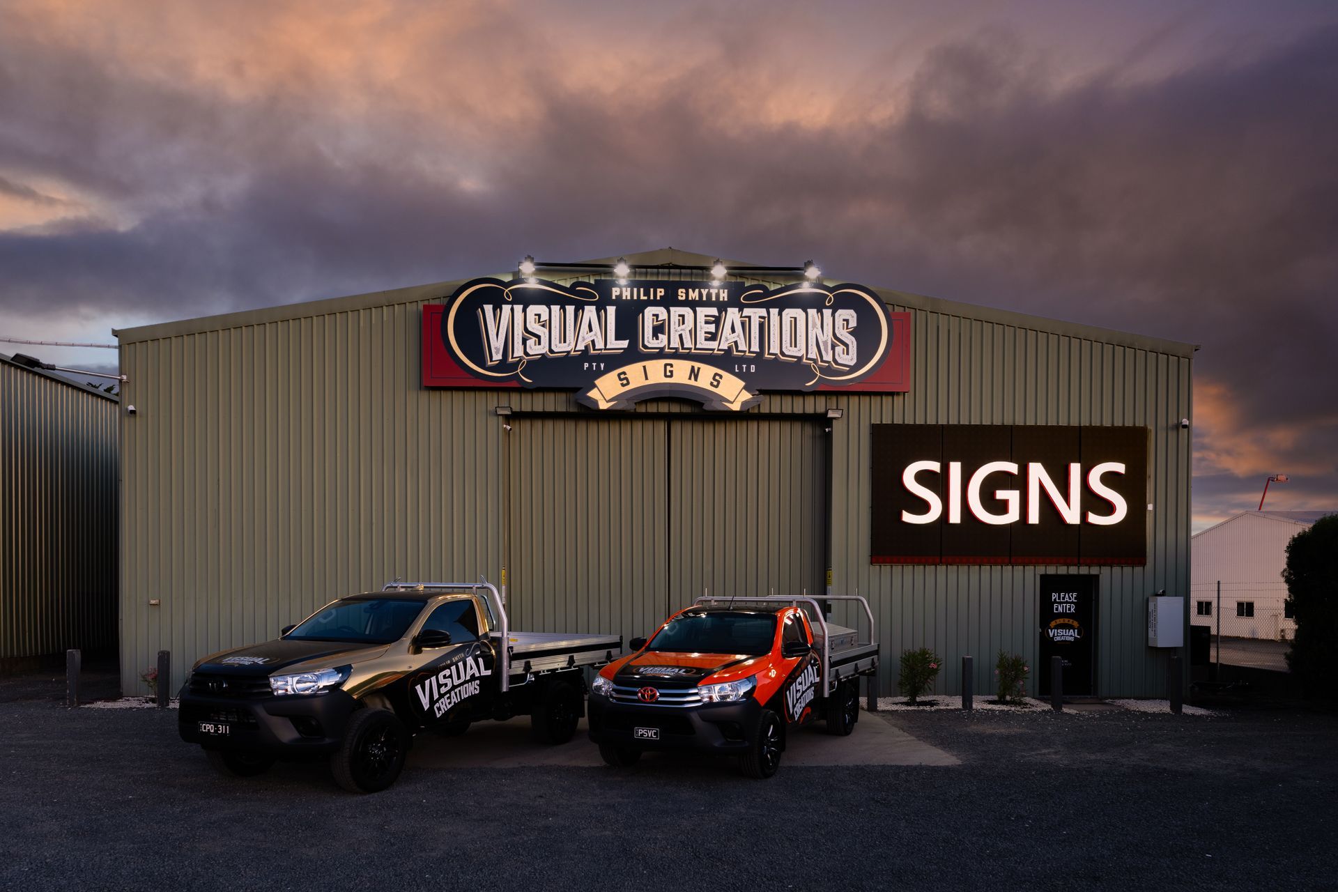Two trucks are parked in front of a building that says visual creations