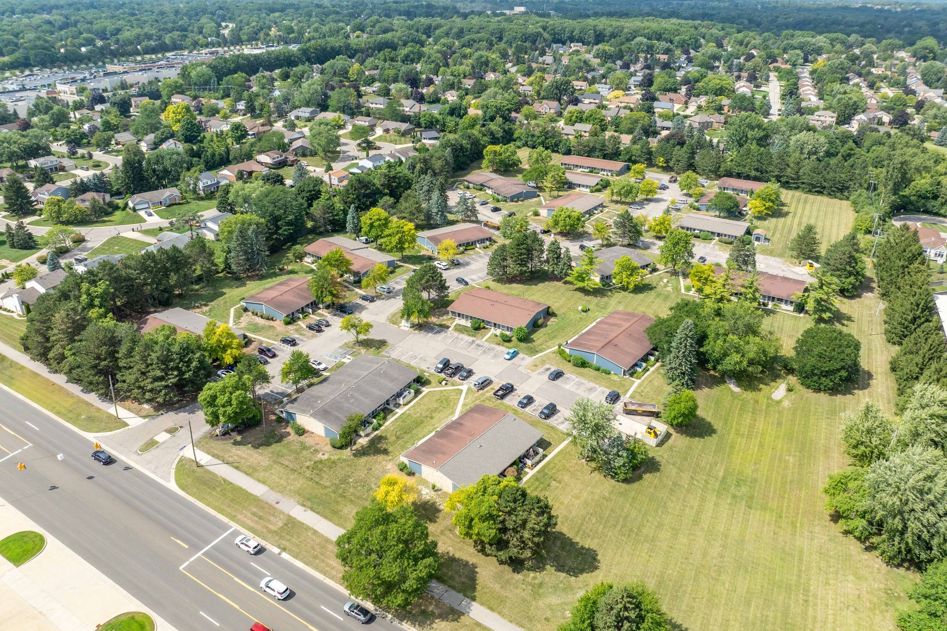 Aerial view of a suburban neighborhood with rows of houses, green trees, and a road.